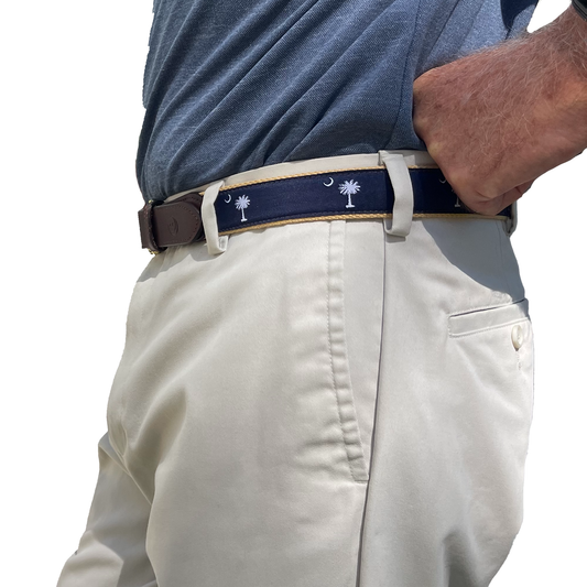 Person wearing a navy belt with palm tree design on beige pants against a white background
