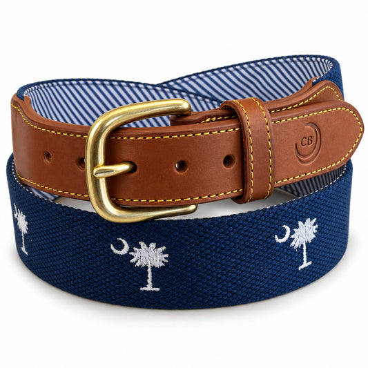 A navy blue canvas belt with white embroidered palm trees and crescent moons, featuring a brown leather strap and a gold buckle. The brand logo 'CB' is embossed on the leather keeper. sc flag belt.