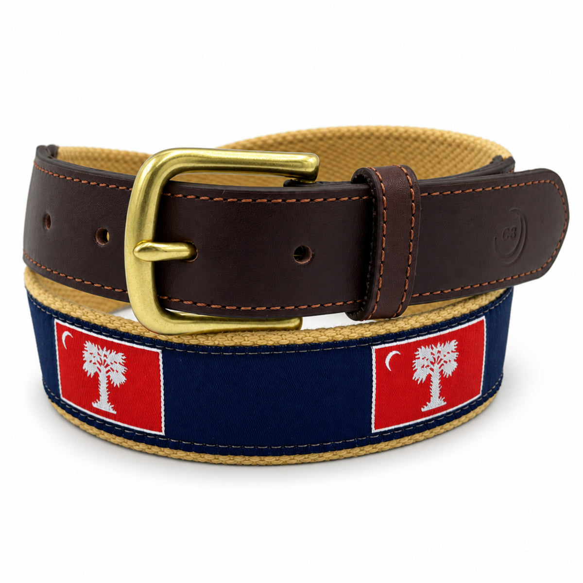 A coiled belt featuring a dark brown leather strap with a gold buckle, a navy blue canvas outer band with two red The Citadel Big Red flags, and a tan woven inner lining, shown on a white background.