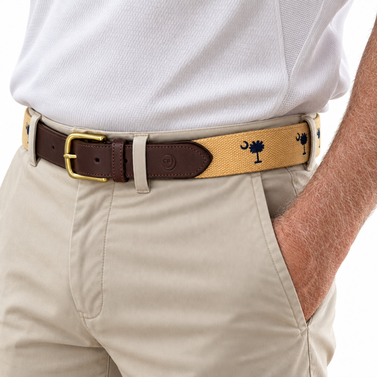 A close-up of a person wearing a tan woven belt with dark brown leather trim, a gold buckle, and navy blue South Carolina flag the crescent and palmetto, paired with khaki pants and a white polo shirt.
