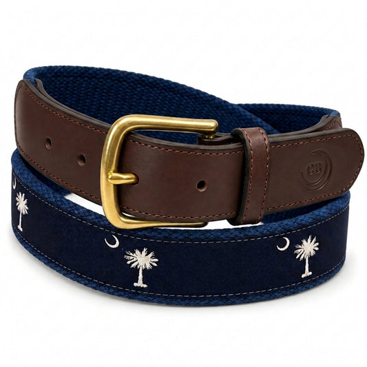 A South Carolina flag crescent and palmetto belt featuring a navy blue canvas body with white palm tree and crescent moon embroidery, a brown leather strap, and a gold buckle.