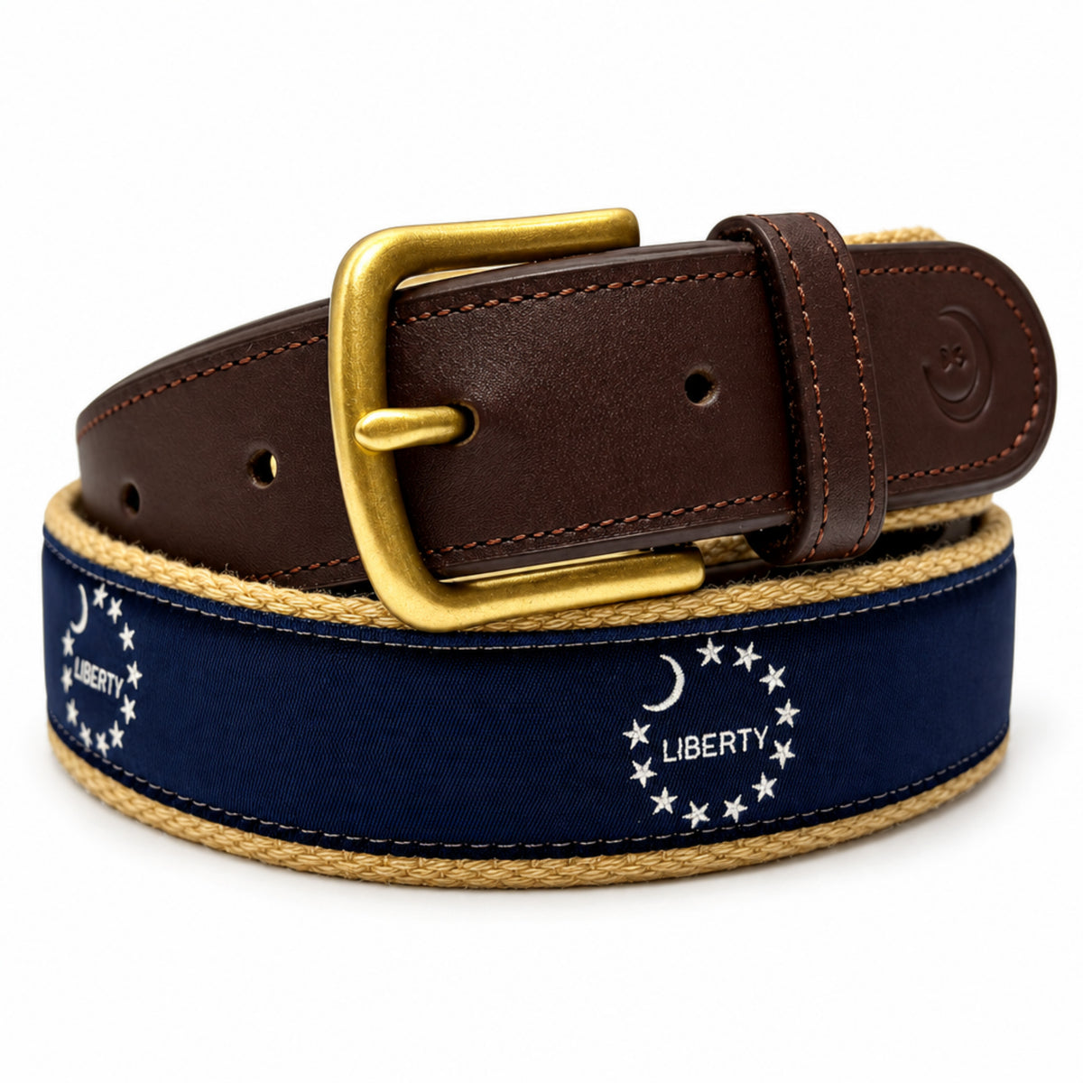 A navy blue canvas belt with a gold-tone buckle, brown leather end, and a braided beige rope edge. The canvas features a white embroidered circle of stars and the word 'LIBERTY' with a crescent moon.