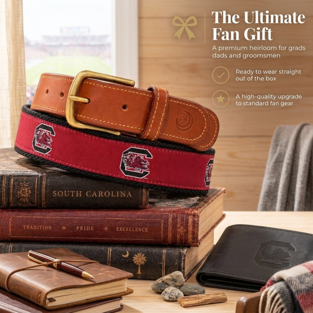 A South Carolina Gamecocks-themed fan gift set featuring a brown leather belt with a gold buckle and a red woven belt with South Carolina C logo and text, styled on a stack of vintage books with a notebook, pen, stones, and wallet nearby. Text on the right reads 'The Ultimate Fan Gift' with product features.