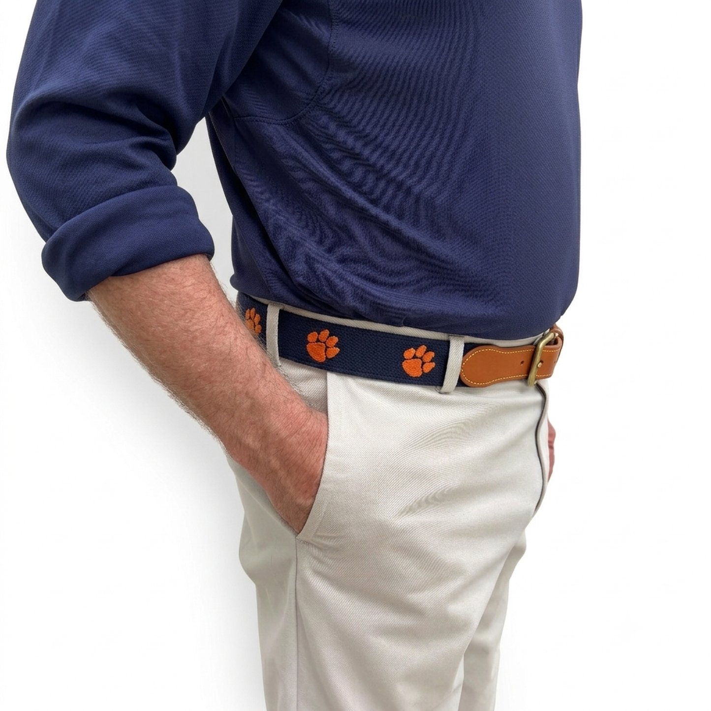 A close-up of a person wearing a navy blue polo shirt, white pants, and a matching navy belt with orange paw print motifs and a brown leather buckle.  Clemson Tigers officially licensed logo and team name.