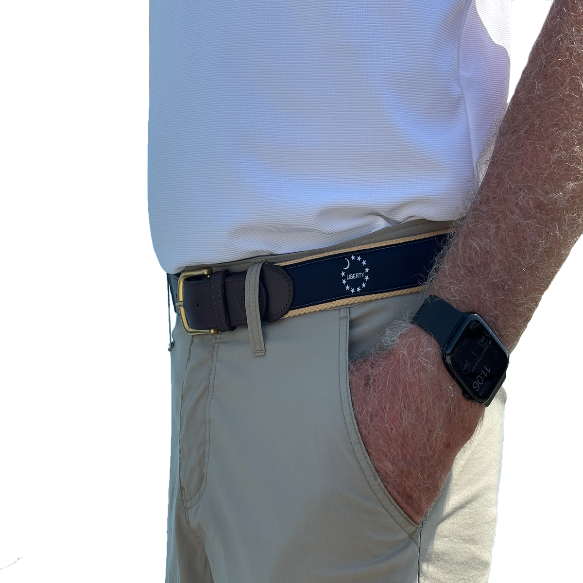 A close-up of a man wearing a dark navy golf belt with a gold buckle and a white embroidered logo, paired with khaki pants and a white polo shirt.