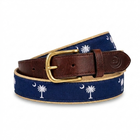 A navy blue canvas belt with a white palmetto tree and crescent moon pattern, the south carolina flag insignia, featuring a brown leather strap, gold buckle, and a beige khaki canvas web backing. 